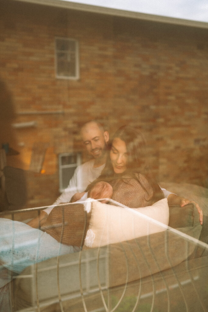 Parents holding baby Maisie in a sun-drenched living room.