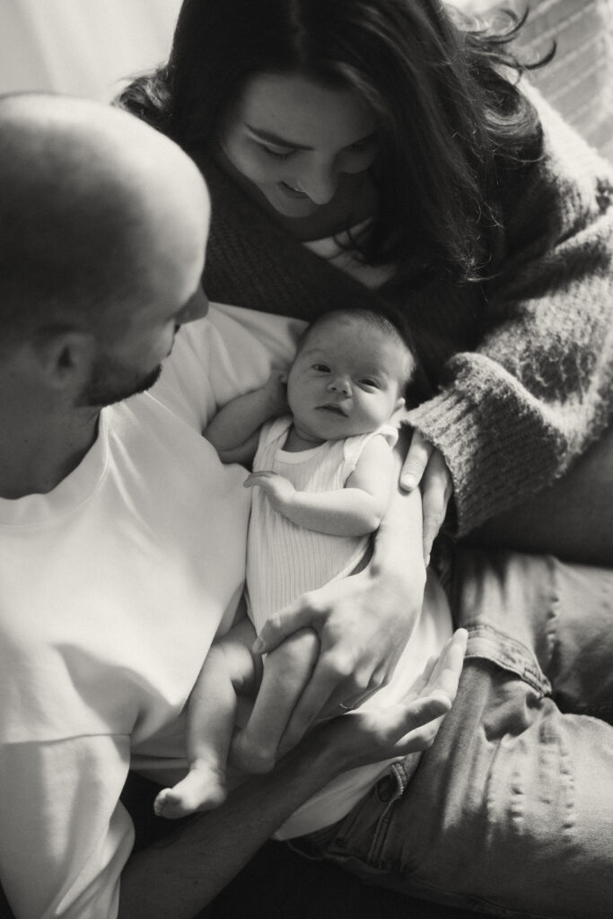 Parents holding baby Maisie in a sun-drenched living room.