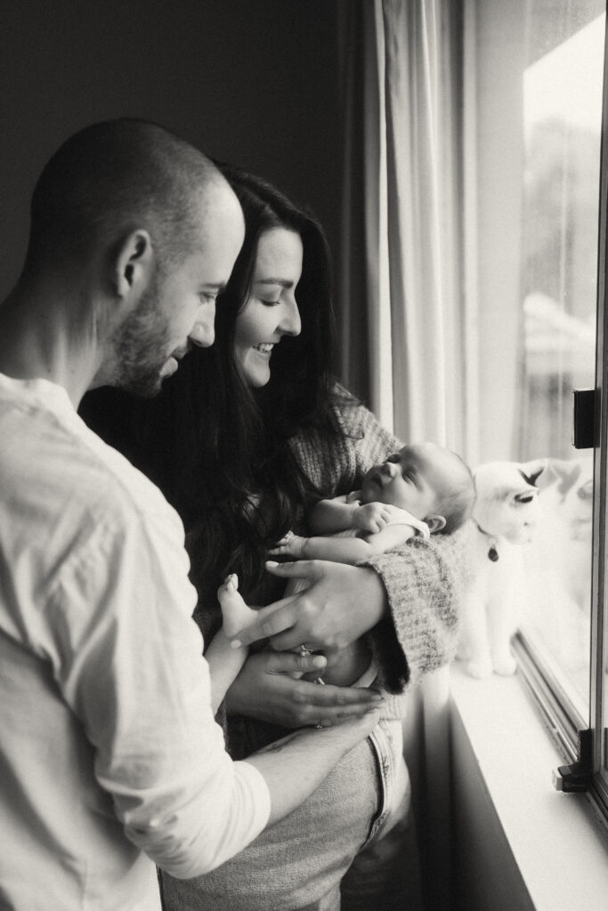 Parents holding baby Maisie in a sun-drenched living room.