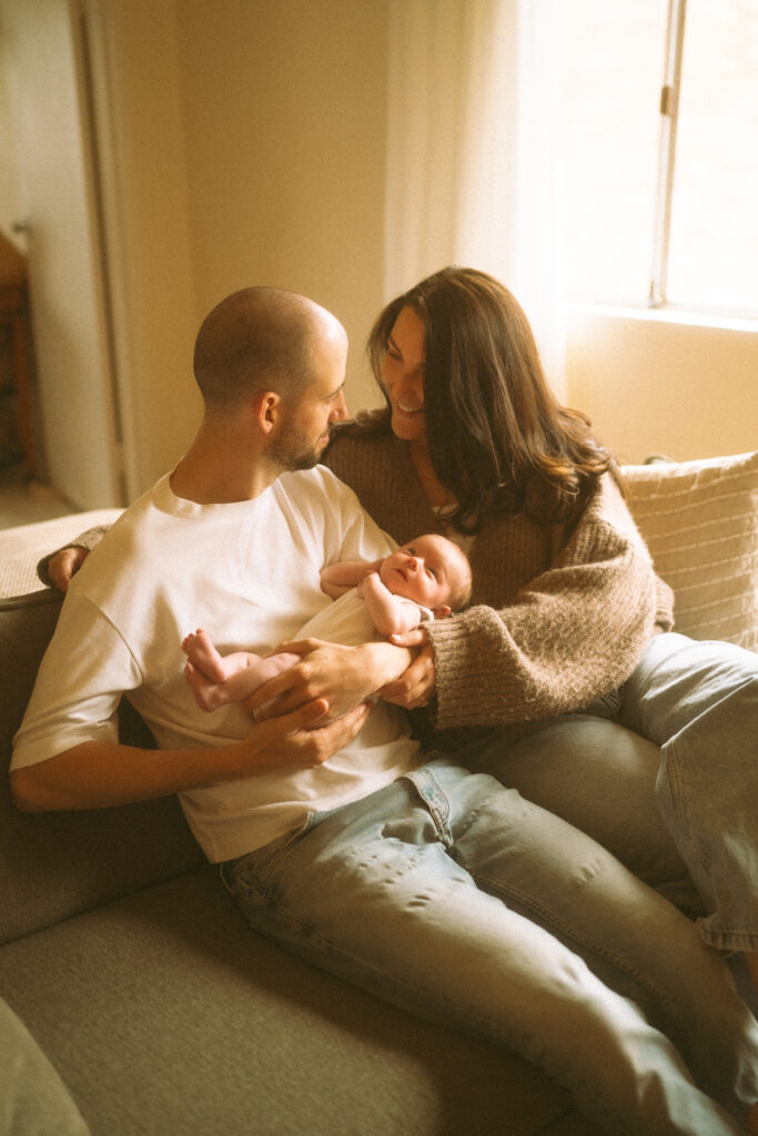 Parents holding baby Maisie in a sun-drenched living room.